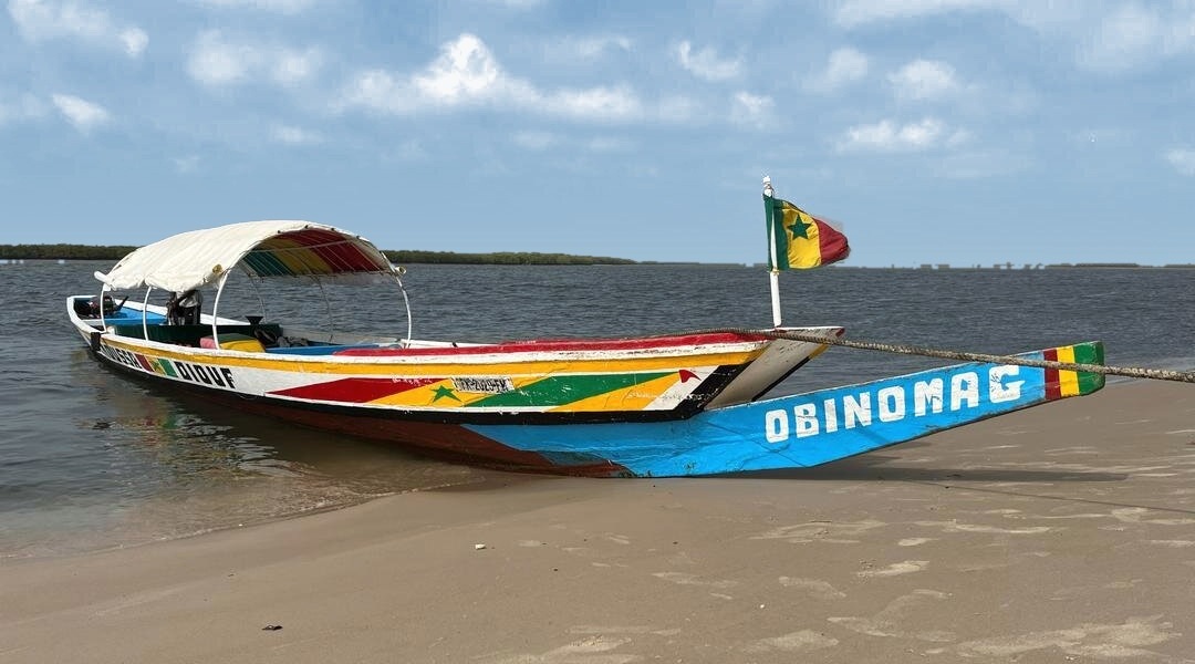 La pirogue Obinomag, proue bleue et taud tricolore, sur une plage du Sine Saloum